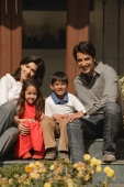 family of four sitting front doorstep, smiling at camera - Alex Mares-Manton