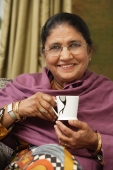 older woman with glasses holds cup of tea, smiles at camera - Alex Mares-Manton