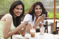 two young women having drinks,holding cell phones - Vivek Sharma
