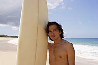 man standing next to surf board on the beach - Yukmin