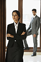 businesswoman with folded arms, businessman in background - Alex Mares-Manton