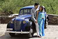 young couple looking at each other in front of blue antique car - Alex Mares-Manton
