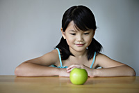 Little girl at table looking at green apple - Yukmin