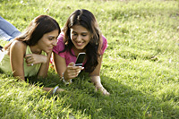 two teen girls in park, looking at text messages - Alex Mares-Manton