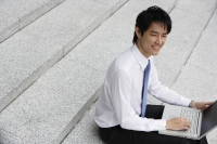 Businessman sitting on steps ans working on laptop - Yukmin
