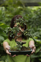 Young woman holding up bonsai tree - Nugene Chiang
