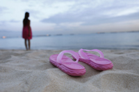 Sandals on sandy beach, woman in background - Yukmin