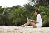 Young woman working on laptop on beach - Yukmin