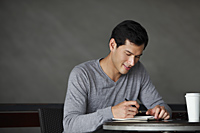 man writing in a book, smiling slightly - Yukmin