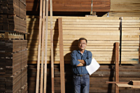 Mature man leaning against a stack of lumber. - Nugene Chiang