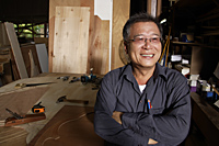 Smiling mature man in front of his work bench. - Nugene Chiang