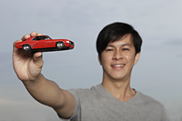 Young man holding up red toy car - Yukmin