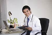 Doctor sitting at desk working on computer, smiling - Yukmin