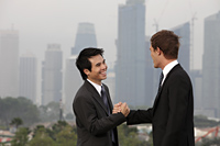 Chinese and Caucasian man shaking hands in front of city sky line - Yukmin