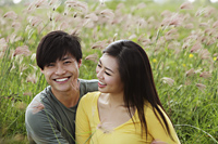 young couple sitting in field together laughing - Yukmin