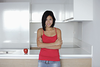 young woman standing in kitchen with an apple, wearing red top - Yukmin