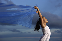 young girl holding up blue cloth, blue sky background - Yukmin