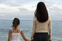 Rear view of mother and daughter holding hands looking at the water - Yukmin
