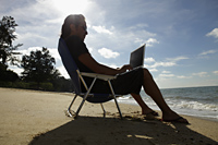 Man sitting on beach chair working on laptop at the beach - Yukmin