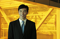 Young man smiling and wearing a business suit standing in front of orange tinted glass - Yukmin