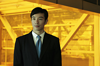 Young man wearing a suit standing in front of orange tinted glass - Yukmin