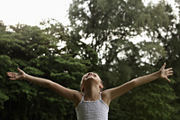 Young girl with arms outstretched looking up at the sky smiling, trees background - Yukmin