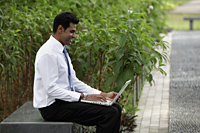 Indian man sitting outside working on laptop with plants in background - Alex Mares-Manton