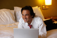 man lying on bed smiling while working on lap top - Yukmin
