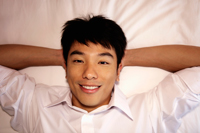 close up of man laying on bed with hands behind his head and smiling - Yukmin