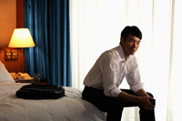 Young man sitting on edge of bed in hotel room - Yukmin