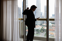 Man wearing suit, looking at phone near window - Yukmin