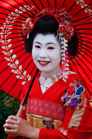 Head shot of Japanese woman in traditional makeup holding red umbrella. - Travelasia