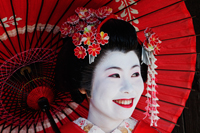 Japanese woman in traditional clothes, smiling and holding red umbrella - Travelasia