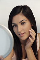 Head shot of young woman holding mirror and touching her face - Alex Mares-Manton