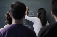 Rear view of students watching teacher write on chalk board - Alex Mares-Manton
