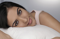 Close up of young woman resting on pillow looking at camera - Alex Mares-Manton