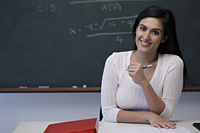Young teacher sitting at desk in front of chalkboard and smiling - Alex Mares-Manton