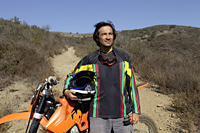 Man standing in front of motorcycle in front of dirt road - Yukmin