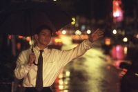 Male executive hailing taxi with umbrella in rain at night - Alex Microstock02