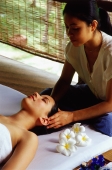 Asian masseuse massaging temples of Eurasian female lying down - John McDermott