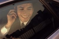 Male executive using cellular phone in car, smiling - Jade Lee