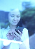 Young woman standing behind window, writing on palmtop - Jade Lee