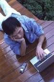 Young man lying on floor, using laptop - Jade Lee