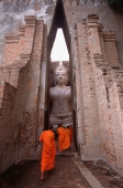 Thailand, Sukothai, Monks stand before a giant statue of Buddha - John McDermott