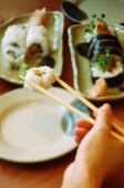 Hand holding chopsticks picking up sushi - Keith Brofsky