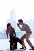 Couple by waterfront, man holding video camera - Gareth Brown