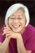 Mature woman leaning chin on hands, laughing, portrait - Mary Grace Long