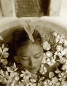 Woman in bath with floating flowers, head under running water - Jack Hollingsworth