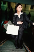 Woman on escalator, carrying shopping bags - Gareth Brown