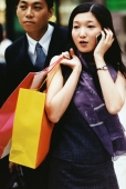 Couple walking together, woman with shopping bags using cellular phone - Jade Lee